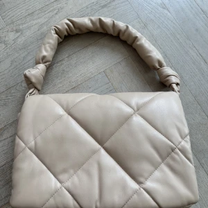 STAND STUDIO Wanda mini bag - Quiltad fold-down clutchväska från Stand Studio gjord i en fin fauxläder-kvalitet. Väskan stängs med tryckknappar, har en innerficka med dragkedja och levereras med ett handtag.  Mått: H 20 cm, B 30 cm, D 7 cm. Handtaget 55 cm.  Material: 50% polyuretan, 