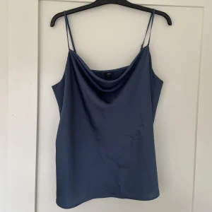 Topp  - En blå topp i satin. Väldigt smickrande, hänger väldigt fint på. Har tyvärr blivit för liten för mig. Den har blivit snaggad på vänster sida, men det är inte tydligt. Eu 42/UK 16. Skriv om fler bilder eller frågor!💗