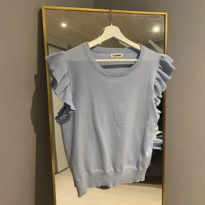 Stickad tröja - Fin ljusblå stickad T-shirt/linne med volang. Helt oanvänd. Hör av er för fler bilder eller funderingar💙