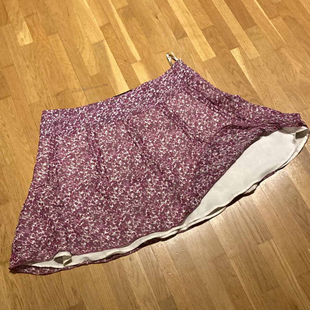 Lila blommig kjol med vit innerkjol Dragkedja i sidan . Hameet.