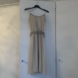 Beige klänning - Gullig beige klänning som går ner till knäna på mig som är 160 cm lång. Den har även ett pärlat bälte och pärlade detaljer runt kragen. Använd endast en gång.