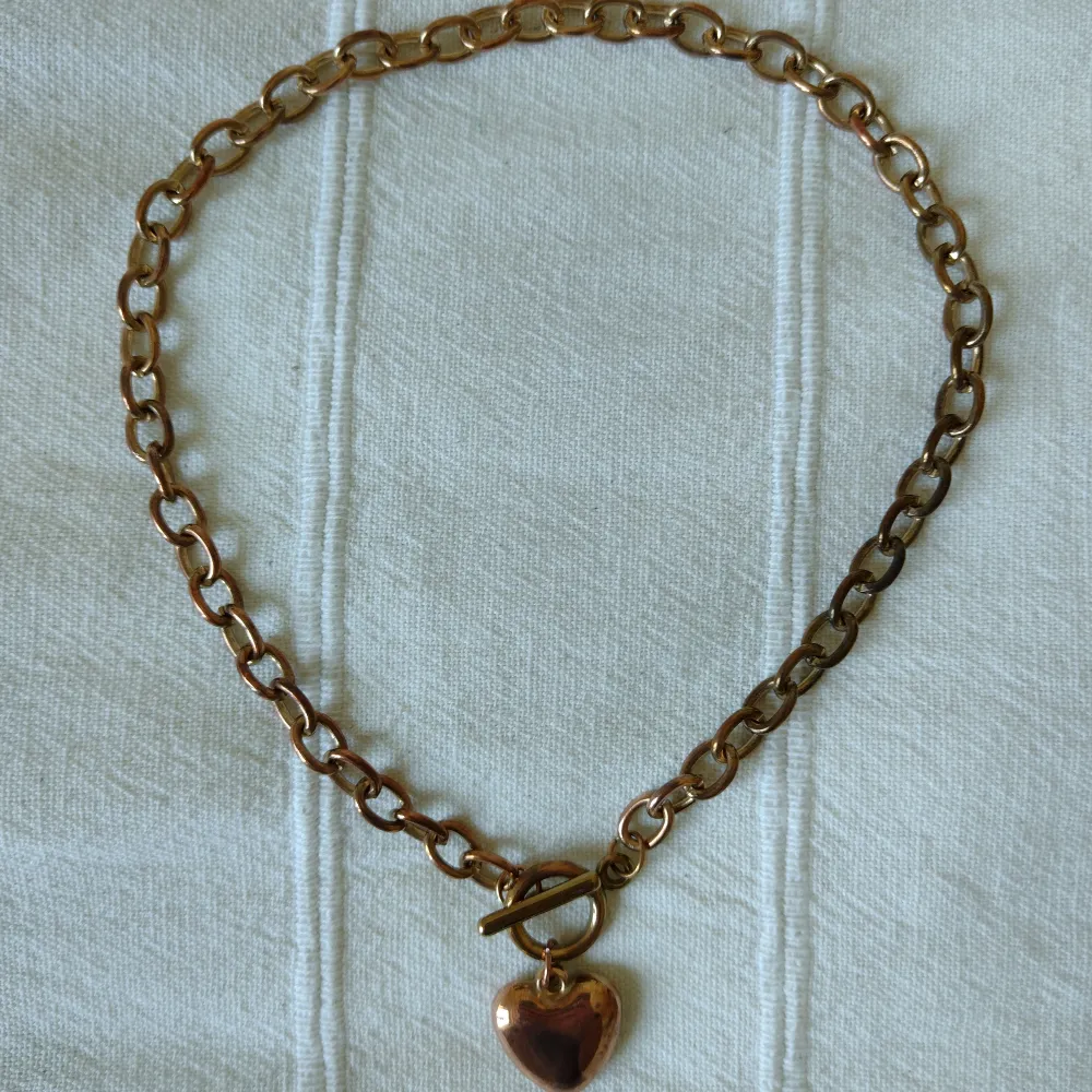 Halsband i metall med berlock i form av ett hjärta. Ca 40 cm långt. Mässings-/kopparfärgat - färgen skiftar lite. Kan skickas med ett frimärke (18 kr).. Accessoarer.