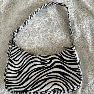 Väska  - Hej! Säljer nu min zebra mönstrade väska då den aldrig kommer till användning. Använd fåtal gånger så är som nyskick! Bild Nr 2 är för att få en uppfattning om storleken, rymmer mobil + fler saker! Köparen står för frakten!🥰