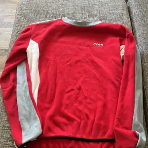 En röd peak performance tjock tröja i bra skick. Den e vintage då den är 20 år gammal men är knappt använd och är i bra skick. Är egentligen för män men funkar för alla 🥰