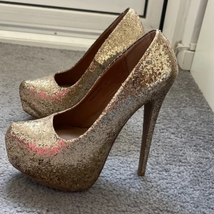 Glittriga klackskor  - Guldglittriga klackskor, oanvända.