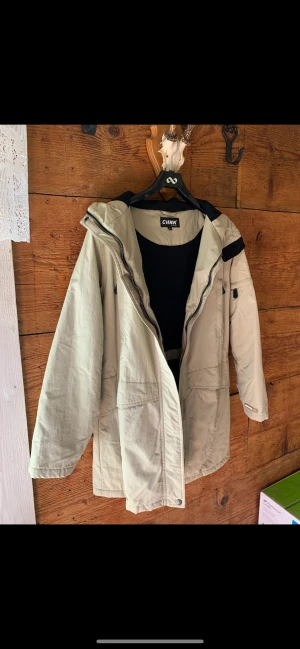 CHNK By CHINOOK. Jacka / Parkas. St: 38 -40. - Fin Vår och Höstjackan. Färg: Ljus beige. Mått: från ärmhåla till ärmhåla: 2 x 55 cm. Från ärmhåla till nederkant: 57 cm. Hel längd bakstycke: 82 cm.  Skickas med Post Nord spårbart: 72 kr.