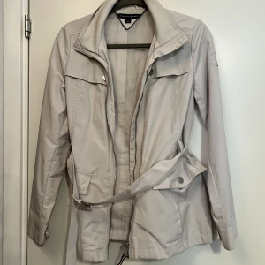 Vår jacka - Tommy hilfiger jacka. Kräm vit färg. Använd en del gånger. Har ett bälte runt midjan. Fint skick.