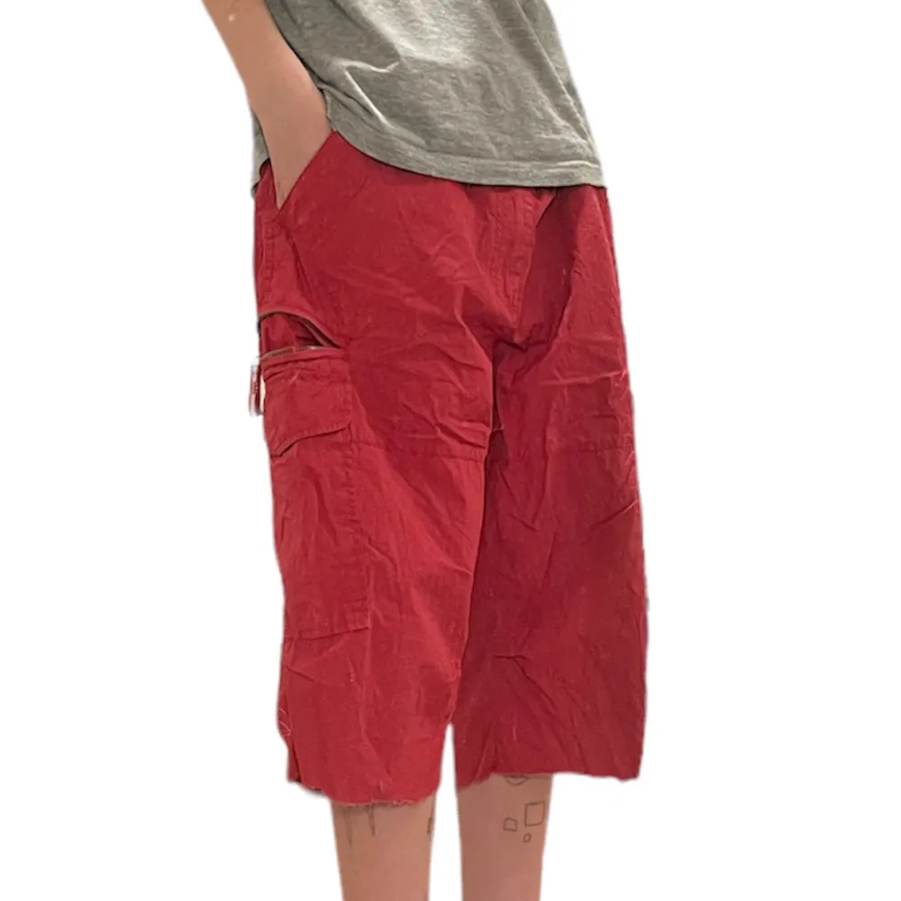 Ett par röda shorts med en mängd praktiska fickor. Avklippta i nederkanten samt flitigt använda, dock inga större defekter. Midja: 87cm. Innerbenslängd: 35cm. Benbredd: 29cm. Vid frågor eller önskemål om fler bilder, skriv privat!. Shorts.