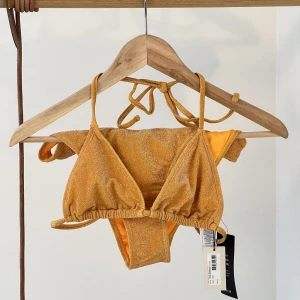 Glittrig bikini - En orange glittrig bikini ifrån NA-KD. Aldrig använd så är i super bra skick!   Bikini toppen är i storlek XS och underdelen i storlek S