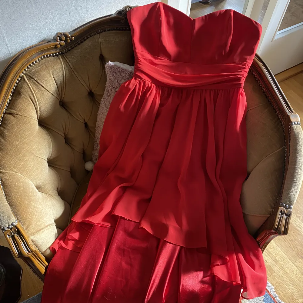 Röd klänning som är kortare fram och lång bak. Band och storlek är bortklippt för att inte sticka upp när den bars.. Klänningar.