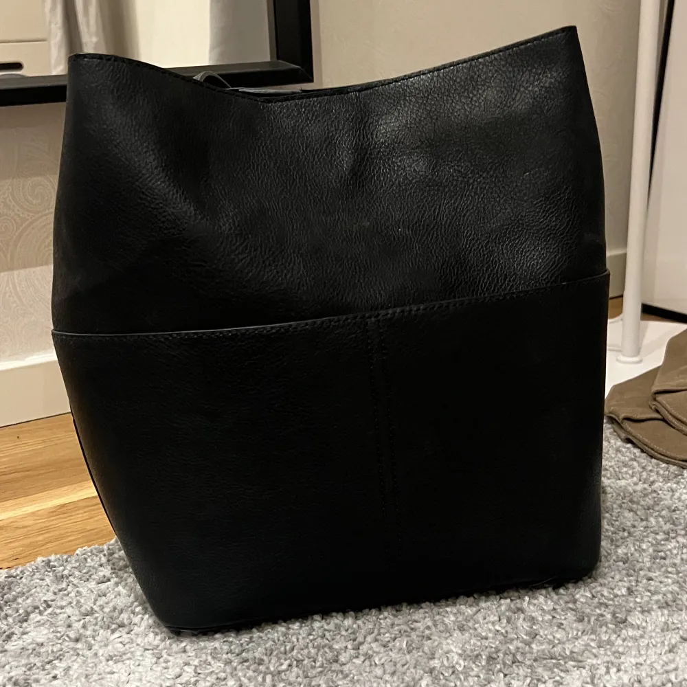 En svart väska i läder från Åhléns, mycket rymlig med en avtagbar organiseringsficka. Väskan är i nyskick och perfekt för skolan❤️. Väskor.
