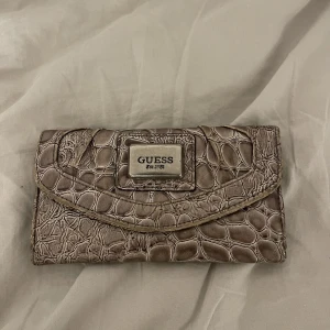 Guess plånbok - Guess plånbok i ormskinn i en brun beige färg med silverdetaljer:)