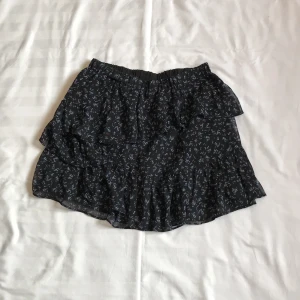 Blommig svart volangkjol  - - Plagg: Kjol - Mönster: Blommig  - Färg: Svart (blommor är blåa & rosa) - Storlek: M - Märke: Stradivarius  - Skick: Mycket bra  - Egenskaper: Blommig, kort, volangkjol,  Kontakta mig gärna vid frågor 💕 