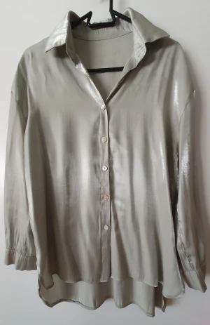 Glansig lång blus - Grön glansig blus i polyester Storlek 36 Längd baksidan 73 cm, framsidan ca 63 cm. Rundad avslut neråt. Djur och rökfritt hem.