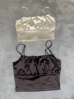 Två satintoppar - En vit och en brun satintoppar.Är jättesköna på, passar perfekt för en mer kanske festligare eller mer ”finare” tröja att välja 🤍🤎har inte använt dom alls mycket bara testat men kunde ej lämna tbx de, passar jättefint med ett par Jeans ex, 20kr styck