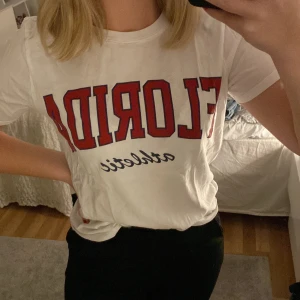 T-shirt  - T-shirt från ginatricot i storlek s, står ”Florida athletic” på bröstet i röd och mörkblå färg. Är oversized i passformen. 