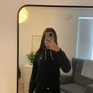 Polo Ralph Lauren svart hoodie - Hoodien är använd men fortfarande i bra skick. Hoodien är svart/ grå och har en vit logga format som en polo spelare vid bröstet. Jag är 170 cm och hoodien har en lite kortare passform med långa ärmar. Nypris 900kr.