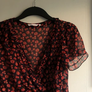 Blommig klänning - Säljer en blommig klänning i rött och blått med volang nertill! Materialet är typ som mesh, 100% polyester. Skick: köpt second hand och använd en gång själv! Storlek 40 men beroende på önskad fit så passar den xs-large skulle jag säga! 