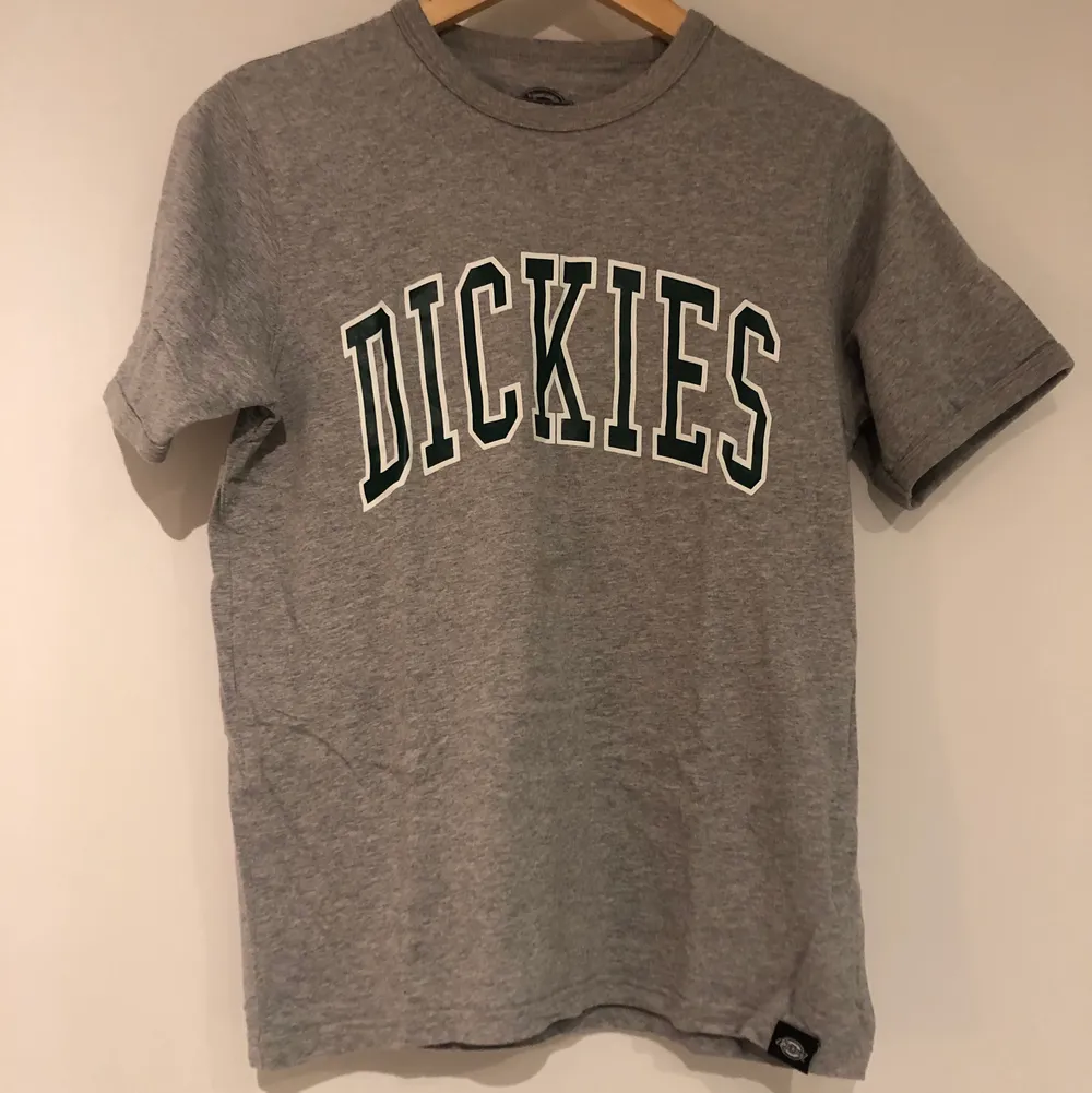 Grå t-Shirt med tryck ”Dickies”. Varan har inga tydliga defekter. Jag är 168cm lång för referens. Plagget har funnits i hem där hund finns. Meddela om pris eller frakt vill diskuteras eller om fler bilder vill has. . T-shirts.