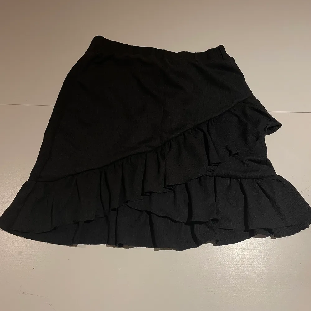 Det är en svart kjol med volanger. Stretchigt material. . Kjolar.