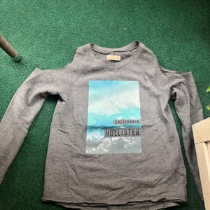 Tuff sweatshirt från Hollistet - Snygg sweatshirt från Hollistet. Nyskick.Använd endast 1-2ggr. Superskön i kvaliten. Tufft motiv framtill och öppna axlar. Stl xs.
