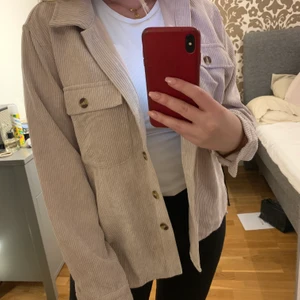 Corduroy Skjorta - Skjorta i mamchesterliknade material. Storlek S. Ljusrosa färg och tunt material. Passar som lättare jacka till sommaren. Beigerosa färg