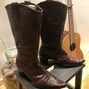 Bruna Stövlar stl 38 - Jättecoola typ ”cowboy” stövlar 👢 i brun ormskinns imitation stl 38. Nästintill oanvänt skick! Inköpta för något år sedan, jättefina som boots till en kjol tillexempel!