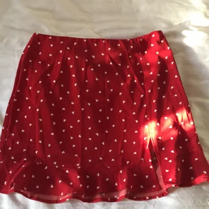Helt ny röd kjol med vita hjärtan - Helt ny röd kjol med små vita hjärtan på. Har en liten slits och liten volang. Finns dragkedja på sidan. Storlek M passar även S🥰