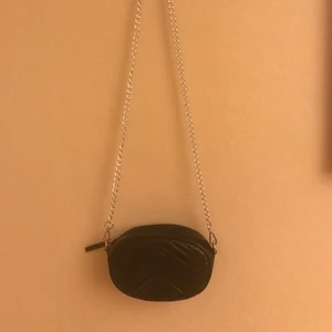 Axelväska/midjeväska - En svart väska som både kan andvänds som en axelväska och en midjeväska då det tillkommer skärp. Aldrig använd och i fint skick. Det är en oval formad väska med sicksackande skinnimmation tyg. 