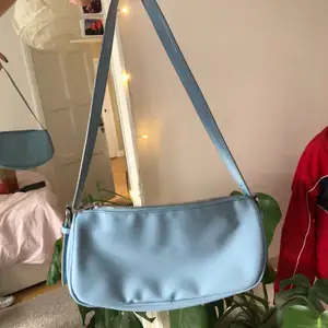 En babyblå vinyl baguettebag köpt från Nelly. Har en fläck (se bild 3)  som inte märks mycket alls om man inte kollar noga. Silvriga detaljer, dragkedja och har en ficka inuti. Skriv för fler bilder eller frågor!!!