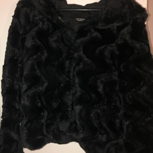 Svart pälsjacka - En svart fake päls jacka med stor luva i storlek M men funkar även för storlek S. Använd 1 gång.