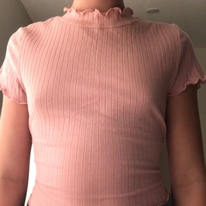 En rosa t-shirt - Köp den här fina rosa t-shirten. Den har volanger på nedre delen av tröjan och vid armarna och vid halsen. Den är använd 2 gånger men om ni beställer den får ni den tvättad när ni får hem den.
