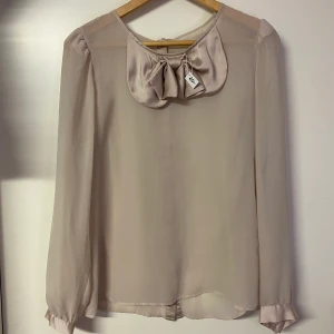 Beige blus - Beige/ljus rosa blus med rosett framtill och knappar i ryggen, storlek S. Frakt tilkommer
