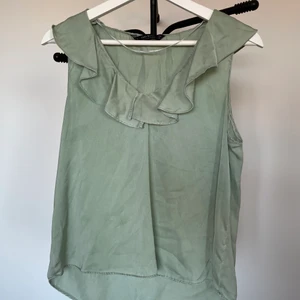 Topp - Söt ljusgrön topp i silkesliknande tyg! Fina volanger i halsringningen som gör den lite festligare. Storlek S men eftersom materialet inte är stretchigt så är den lite tajt över bysten. Frakt tillkommer!