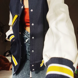 Varsityjacka - Fin Varsityjacka/baseballjacka med vita armar i läder imitation och mörkblått tyg. Gula detaljer. Är i storlek S. Frakt tillkommer. Högsta bud just nu: 350 om du vill bjuda över så gör gärna de i kommentarerna 🥰