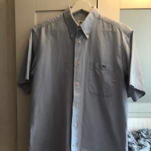 Kortärmad vintage skjorta från Lacoste med oversized passform. Köpt Second hand, i felfritt skick. Vidare ärmar och längre modell. Snygg vintage skjorta.