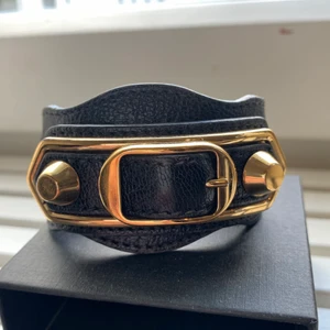 Balenciaga armband - Svart armband från Balenciaga med gulddetaljer! Storlek S men går att reglera själv hur tajt du vill ha det, väldigt bra skick :) 
