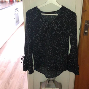 Mörkblå blus med ljusblåa prickar och volangärm. - Mörkblå blus med ljusblåa prickar och volangärmar. Lite större prickar i slutet av ärmen och även ”snöre” i slutet av ärmarna. Knappt använd. 