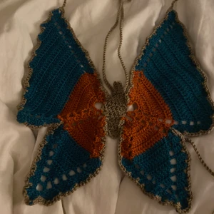 Virkad fjärilstopp  - Virkad topp som är handgjord av mig. Den ska föreställa en fjäril och om ni vill se hur den sitter på kan ni kolla min profil så hittar ni samma topp i mörkblå på mig!             Den går att göra i vilken färg/färger som helst. En färgad kostar 300kr sen blir det ett tillägg på 20kr för varje färg ni önskar att lägga till, t ex toppen på bilden kostar 340kr.