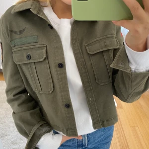 Jacka - Supersnygg militärgrön jacka från Crocker, perfekt till våren ock sommaren! Knappt använd och i mycket bra skick! Den har patches på båda armarna och på baksidan. 