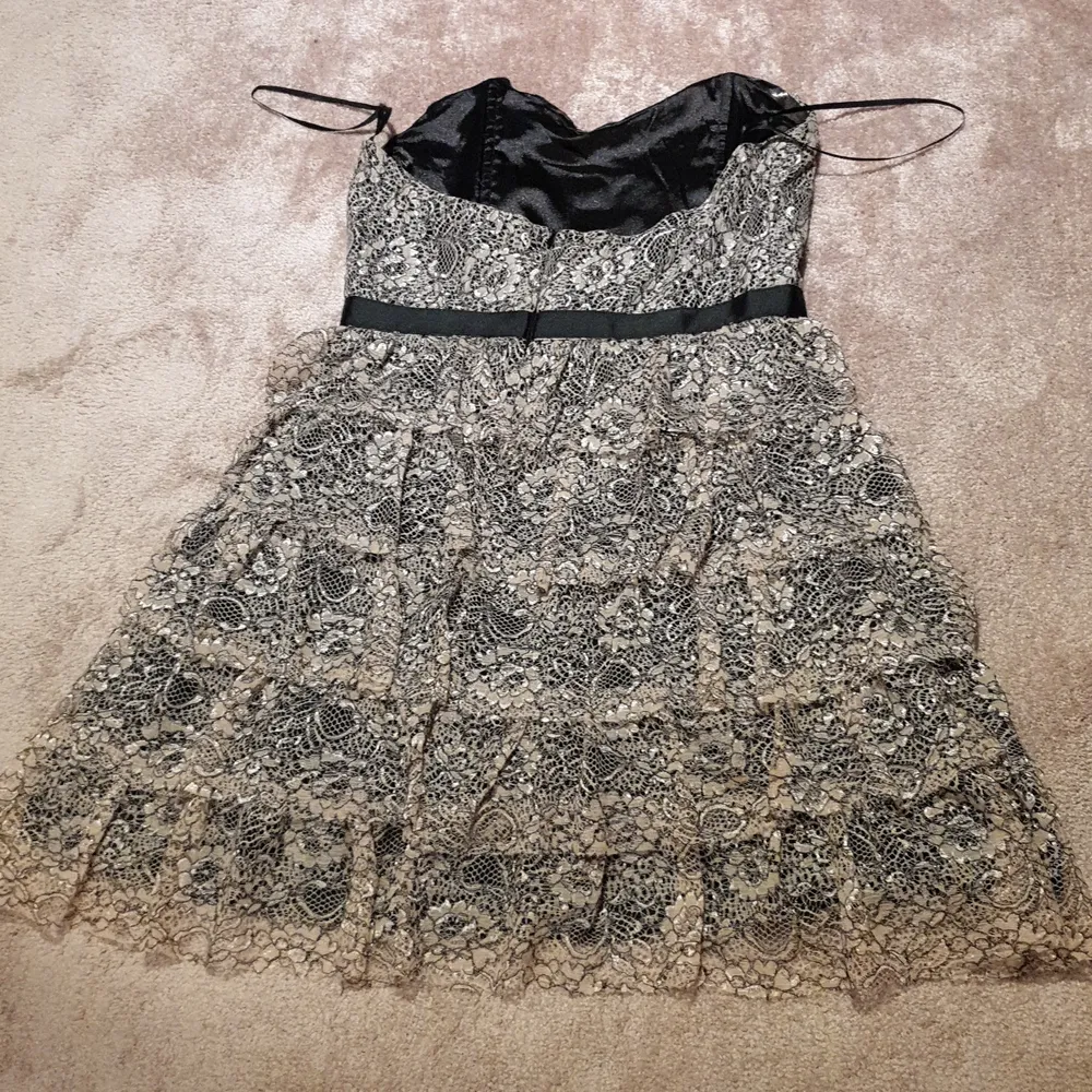 Beige, brun, svart kort volangklänning. Lite större över bysten med tajt kedja kring midjan, passar storlek M också. Polyester. I gott skick. . Mekot.