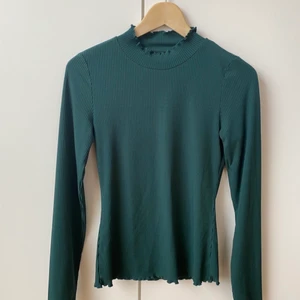 Grön polotopp från Rut & Circle - Snygg grön topp från Rut & Circle. Glansig och med ”volang” i hals, ärmar och nederdel. Storlek S. Använd ett fåtal gånger och jag hittar ingenting att anmärka på. Materiallapp saknas men troligen polyester eller liknande.