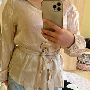 Fin blus i beige - Väldig fin blus med skärp och kragesom passar både vardag och fest. Storleken är M men känns mer som S. OBS: ALDRIG ANVÄND!  (behöver strykas)