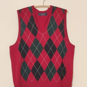 Snygg retro slipover från Pringle of Scotland - storlek XL - Snygg, retro slipover från Pringle of Scotland med ett mönster i röd, grön och vit argyle. Perfekt för nästa jultilfälle!  Skick: Mycket fint vintage-skick Färg: Röd, grön, vit argyle. Storlek: XL Material: 100% Lammull Producerad: Italien  Hör av dig om du vill ha exakta mått eller om du har andra frågor om varan! Avhämtning går att ordna i Lund.