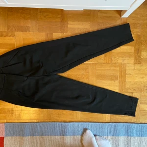 Mjuka svarta kostymbyxor - Mjuka svarta kostymbyxor med resår i svanken. Hög midja. Hylsan för haken saknas (se sista bilden) men har använt ett knapphål istället och det har funkat bra. Köpare står för frakten. 