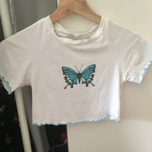Glittrig Butterfly Top - Jättefin crop top i Vitt med blå-glittrigt Fjärilstryck, med blåa detaljer på kanterna. Strlk S men passar någon med lite mindre byst/smalare ribcase. Det svarta är lite blekt men annars gott skick! Kontakt vid intresse eller funderingar ❣️