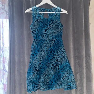 Turkos sommarklänning  - Turkos sommarklänning med leopardmotiv. Endast använd en gång vid skolavslutning. Framtill är urringningen rund men bak är den öppen i mitten med en knapp längst upp. På insidan framtill och i kjolen finns det svart tyg som inte gör den genomskinlig. 