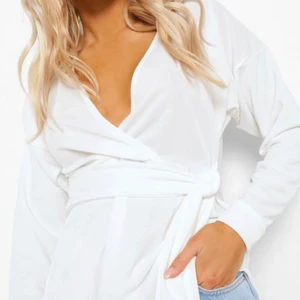 Långärmad omlottblus med knytdetalj i midjan  - En långärmad omlottblus i färgen vit med knytdetalj i midjan. Har aldrig används. Orginal pris 324kr 