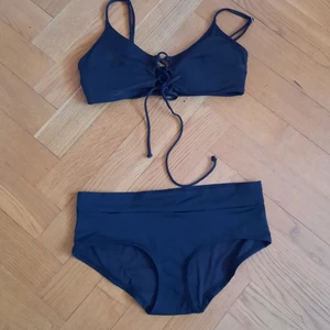 Svart bikini, korsettdetaljer - Svart bikini med korsettliknande snörning på toppen. Underdelen har brett, smickrande band. Den sitter allmänt så smickrande, går att snöra ihop om man inte vill visa jättemycket, men även att sära på lite mer eller möjligen ge en liten push-up effekt utan faktiskt push-up. Kupan är vaderad men inte utbyggd. Toppen är storlek 38, men mpnga då snörningen går att justera och underdelen är i storlek 36.