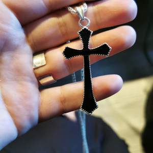 Ett svart kors som hänger på en silvrig kedja (fake)   kedjan är väldigt lång men det går även att byta om man vill ha en annan! 🥰